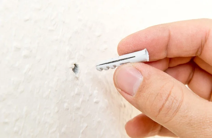 Hand hält einen Dübel vor ein Loch in der Wand